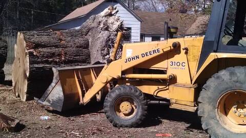 Backhoe moving a large uprooted tree trunk during a storm cleanup