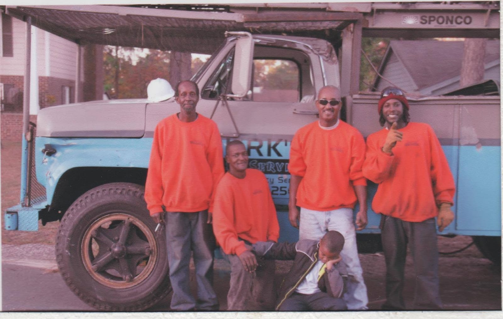 The Burks Tree Service crew in orange shirts standing in front of a company work truck